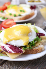 Toast with egg Benedict and tomato on plate on wooden table