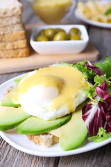Toast with egg Benedict and avocado on plate on wooden table