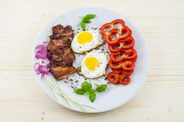 Plate with fried eggs, bacon and paprika on wooden table