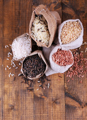 Different types of rice in sacks on wooden background