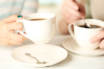 Two women with cups of coffee on bright background