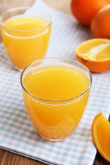 Glasses of orange juice with oranges on wooden table close up