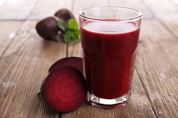 Glass of beet juice with beets on wooden table close up