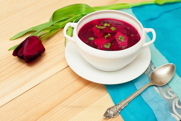 Red soup with dill in white bowl on wooden table with flower tul