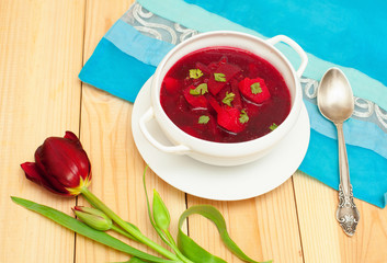 Red soup with dill in white bowl on wooden table with flower tul