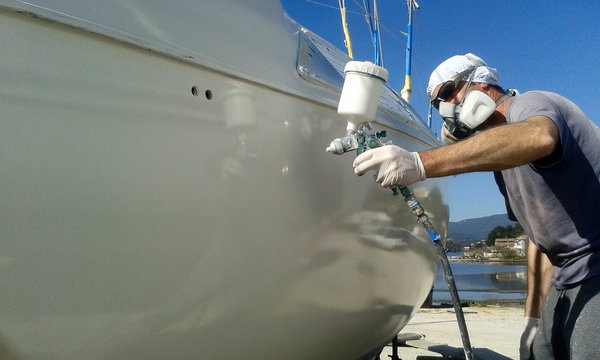 man with face mask spray painting sail boat yacht with air gun	