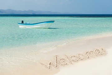 Boat Moored On Sea With Welcome Text Drawn On Sand