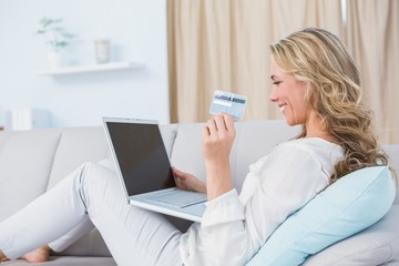 Happy blonde sitting on couch shopping online