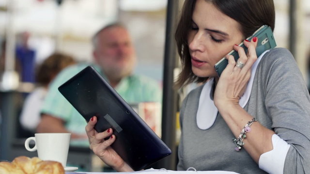 Busy, multitasking businesswoman sitting in cafe in city