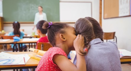 Cute pupils whispering in classroom