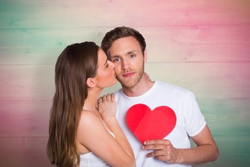 Composite image of woman kissing man as he holds heart