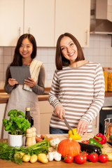 Two smiling female friends are cooking together at home