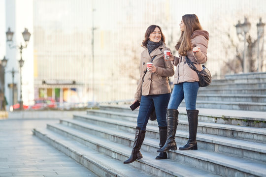 Young Women Walking Down The Stairs Carrying Coffee Cups