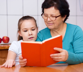 Grandmother is reading book with her granddaughter