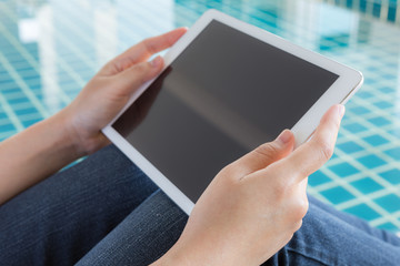 Woman working with tablet sitting at swimming pool