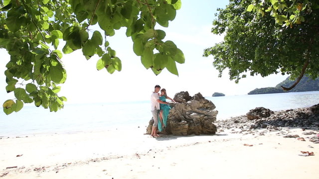ouple of asian blonde girl and handsome guy pose at rock on sand