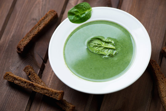 Glass plate with spinach cream-soup on a dark wooden background