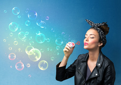 Pretty lady blowing colorful bubbles on blue background