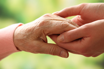 Old and young holding hands on light background, closeup