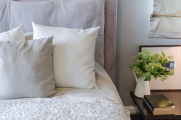 white pillows on white bed with vase of plant on table