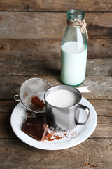 Metal mug and glass bottle of milk with chocolate chunks and