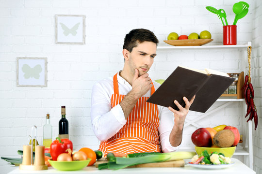Man with recipe book in hands at table with different products