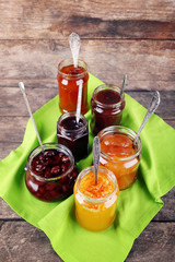 Jars of tasty jam with napkin on wooden background