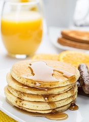Stack of pancakes with breakfast sausage, orange slices, toast, orange juice, and coffee for breakfast