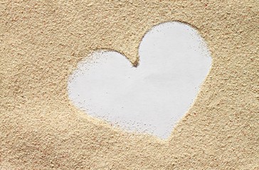 Heart on beige sea sand with paper background