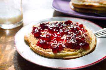 Homemade pancakes with cherry jam on plate and a glass of milk