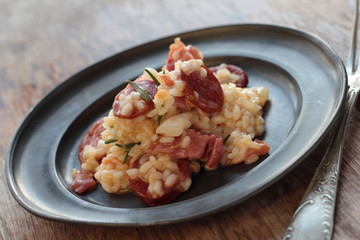 Risotto with sausage, cured ham and rosemary on a tin plate.