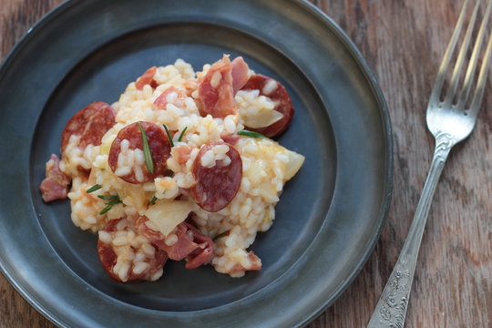 Risotto with sausage, cured ham and rosemary on a tin plate.