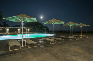 Pool, sunbeds and umbrellas at night