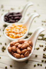 Yellow corn grain and peanut in ceramic spoon on wooden backgrou