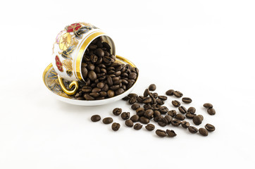 Overturned porcelain coffee cup with coffee beans on white
