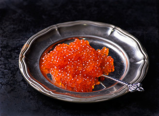 Salmon caviar on metal plate on dark background