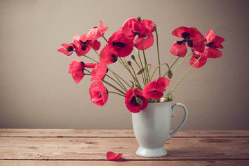 Obraz premium Poppies in cup on wooden table