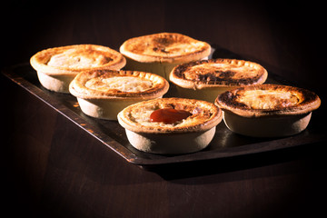 Freshly baked meat pies with sauce and high contrast lighting.