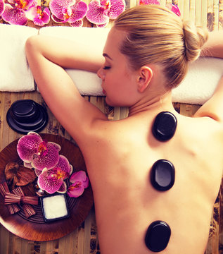 Woman relaxing in spa salon with hot stones on body.
