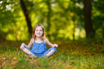 Naklejka na ściany i meble Cute little girl sitting on the grass on summer
