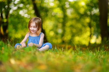 Fototapeta premium Cute little girl sitting on the grass on summer