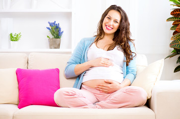 Pregnant smiling woman sitting on a sofa and caressing her belly
