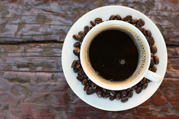 Black coffee in the cup on old wood table with coffee beans