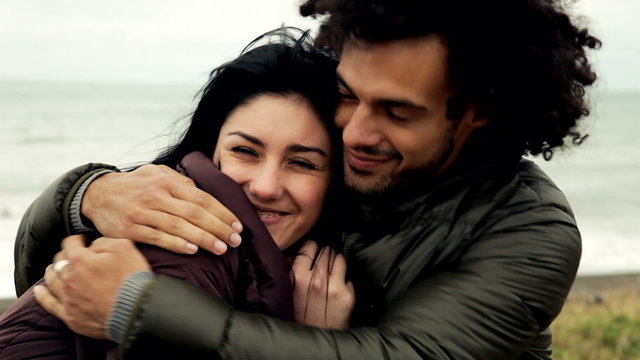 Happy couple cuddling and kissing in winter in front of ocean