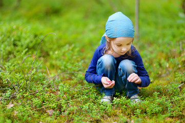 Adorable girl picking foxberries in the forest