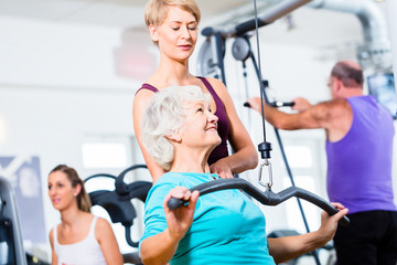 Seniorin beim Rückentraining mit Trainer im Fitness Sport