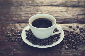 Black coffee in the cup on old wood table with coffee beans