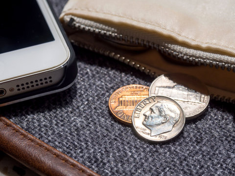 US dollar coins placed outside the wallet with smartphone.