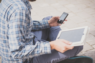 Low section of young man using digital tablet and smartphone outdoors