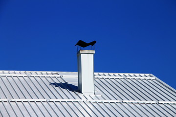 White aluminum roof with chimney against clear blue sky © Ellica